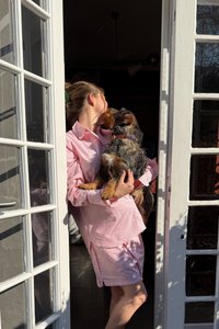 Šviesiai rožinė, dryžuota suknelė su ilgomis rankovėmis ir trumpa apatine dalimi virš kelių. Žmogus laiko mažą šunį, kuris žiūri į jį.