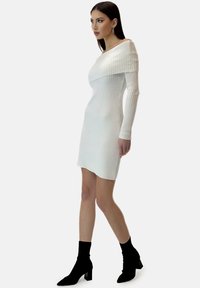 Robe blanche en maille côtelée avec un large décolleté bardot et des manches longues, associée à des bottines chaussettes noires et un ourlet droit.