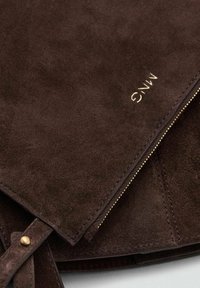 Bolso de ante marrón con un zipper dorado y un logotipo en relieve. La textura es suave, con un diseño limpio y minimalista y herrajes en contraste.