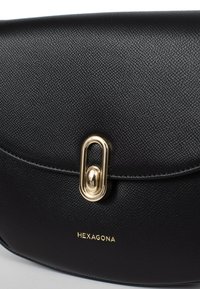 Borsa a mano in pelle nera con texture a granuli, hardware dorato e chiusura a gancio. Presenta il logo "HEXAGONA" impresso sul davanti.