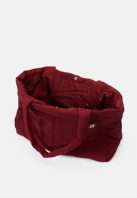 Maroon tote bag made of lightweight fabric, featuring a spacious interior with a zipper pocket, sturdy handles, and a button closure.