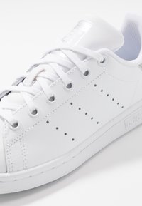 Witte leren sneaker met geperforeerde stippen aan de zijkant, witte veters, gevoerde kraag en een ingedrukte logo op de zool.