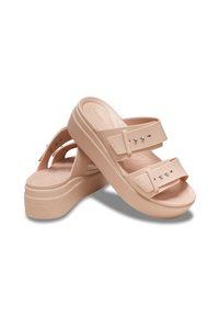 Helle rosa Plattformsandalen mit zwei breiten Riemen, ausgestattet mit dekorativen Metallnieten und einem strukturierten Fußbett für Komfort. Hergestellt aus synthetischem Material.