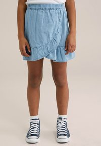 Himmelblauer Denim-Wickelrock mit Rüsche am Saum, elastischem Bund und sichtbaren Nähdetails, kombiniert mit navyblauen High-Top-Sneakers.