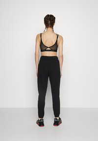 Top sportivo nero cropped con spalline sottili e schiena in rete, abbinato a pantaloni sportivi neri a gamba affusolata, con polsini elasticizzati e vita con cordoncino.
