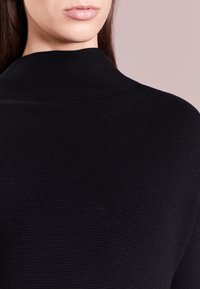 Maglione nero a trama con collo alto. Il tessuto presenta un motivo a coste, creando una silhouette morbida e aderente.