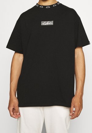 Osoba nosící černé tričko s krátkým rukávem, s malým bílým logem na hrudi a opakujícími se vzory půlkruhu na límci a okraji rukávu.