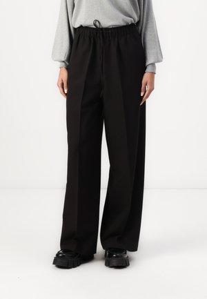 Pantaloni larghi neri con vita a cordoncino, realizzati in tessuto leggero. Abbinati a scarpe nere spesse, creano un fit rilassato.