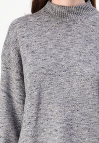 Lys grå strikket genser med ribbestrikket krage. Myk tekstur, litt oversized passform, med subtile flekker av mørkere grått gjennom hele.