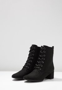 Botas negras hasta el tobillo de ante, con punta afilada, cordones en la parte delantera y un pequeño tacón cuadrado. Cremallera lateral para facilitar su uso.