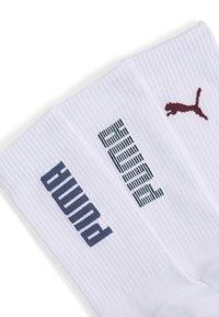 Białe skarpetki prążkowane z ciemnoniebieskim i burgundowym napisem oraz logo "PUMA"; gładka tekstura i długość do połowy łydki.