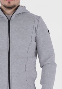 Felpa grigia con zip, realizzata in un tessuto testurizzato, caratterizzata da una zip nera e cuciture curve, con un accento logo sulla spalla.