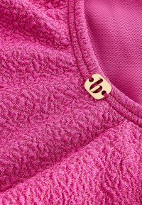 Getextureerde roze stof met een metallic glans, voorzien van een gladde gouden accentknop en een gevarieerd oppervlak dat gebreid lijkt.