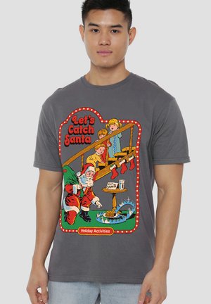 Young man wearing gray shirt with cartoon of children setting a trap with stockings and cookies to catch Santa Claus.
