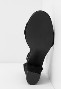 Sandale pour femme noire montrant la semelle lisse et le talon bloc bas texturé sur un fond blanc en coin.
