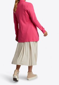 Tajtat rosa kavaj med långa ärmar, parat med en plisserad beige kjol och texturerade beige hög-top sneakers. Slät tyg, skräddarsydd design.