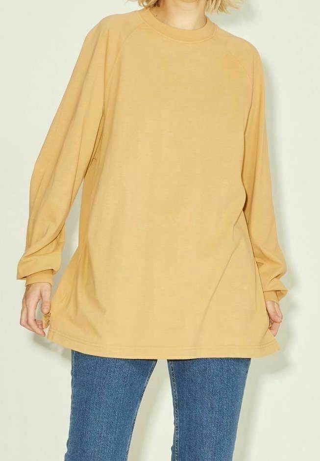 Felpa oversize gialla senape con maniche lunghe a raglan e scollatura rotonda. Tessuto morbido e vestibilità ampia. Abbinata a jeans blu.