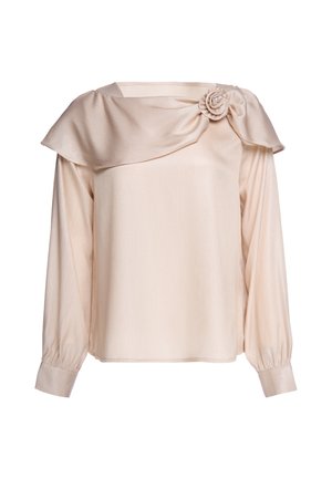 Beige Bluse mit langen Ärmeln, weitem Kragen, der über die Schulter drapiert ist, und dekorativer Stoffblume auf der rechten Seite.