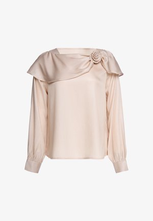 Beige Bluse mit langen Ärmeln, weitem Kragen, der über die Schulter drapiert ist, und dekorativer Stoffblume auf der rechten Seite.