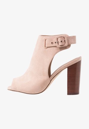 Beige mokkasuoja avotassu korkokenkä, jossa on leikattu muotoilu, leveä nilkkaremmi soljella ja paksu puinen korko.