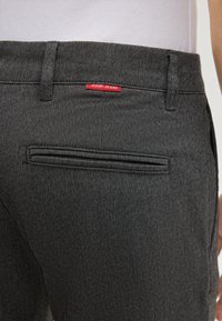 Zbliżenie na szare spodnie w jodełkę z tylną kieszenią welt i małą czerwoną metką "JOOP! JEANS" w pobliżu pasa.