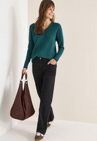 Suéter azul verdoso de manga larga con escote en V, combinado con jeans negros de pierna recta. Bolso de ante marrón y zapatillas marrones con detalles en blanco.