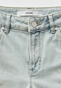 Helleblaue Denim-Jeans mit hoher Taille, ausgestattet mit einem silbernen Knopf und Reißverschluss, auffälligen Nähten und einem Stoffetikett mit der Aufschrift "someday".