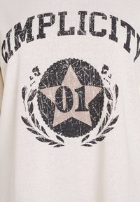 Krēmkrāsas džemperis ar nodilušu uzdruku "Simplicity" vārda, lielas zvaigznes un numura "01" tumšās krāsās ar lauru motīviem.