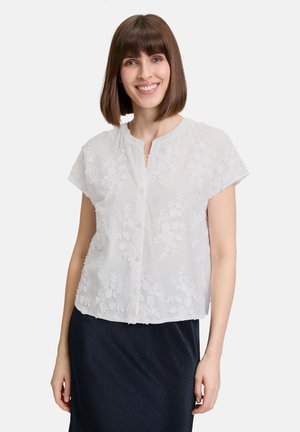Weiße kurzärmelige Bluse mit floraler Stickerei. Sie hat einen runden Ausschnitt und Vorderknöpfe und besteht aus leichtem, transparentem Stoff.