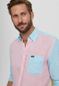 Gestreifte Button-Down-Bluse mit rosa und hellblauen Abschnitten, weißen Knöpfen und einer Brusttasche in hellblau mit einem kleinen Logotag.