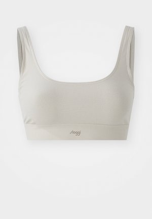 Világos bézs színű, vezeték nélküli melltartó széles pántokkal és sima felszíni textúrával. A melltartó középső alsó részén logó található. Egyszerű dizájn, díszítés nélkül.