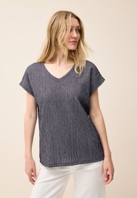 Top de cuello en V de color marino con mangas cortas, que presenta un tejido texturizado con líneas verticales. Diseño holgado para mayor comodidad y transpirabilidad.