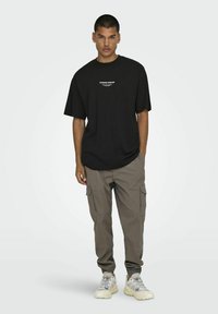 Svart oversized t-shirt med vit text på bröstet, kombinerad med beige cargobyxor med sidofickor och ljusgrå sneakers.