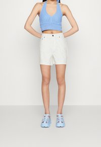 Top de punto azul con tirantes, pantalones cortos blancos con patrón de ojetes y sandalias gruesas de color azul claro con tiras. Vista frontal; adecuado para clima cálido.