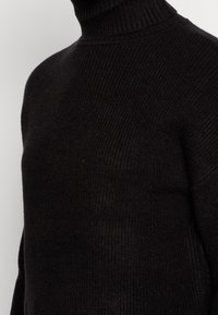 Maglione nero a collo alto con texture a coste. Tessuto morbido, design aderente e colletto alto, adatto per essere indossato a strati durante il clima più fresco.