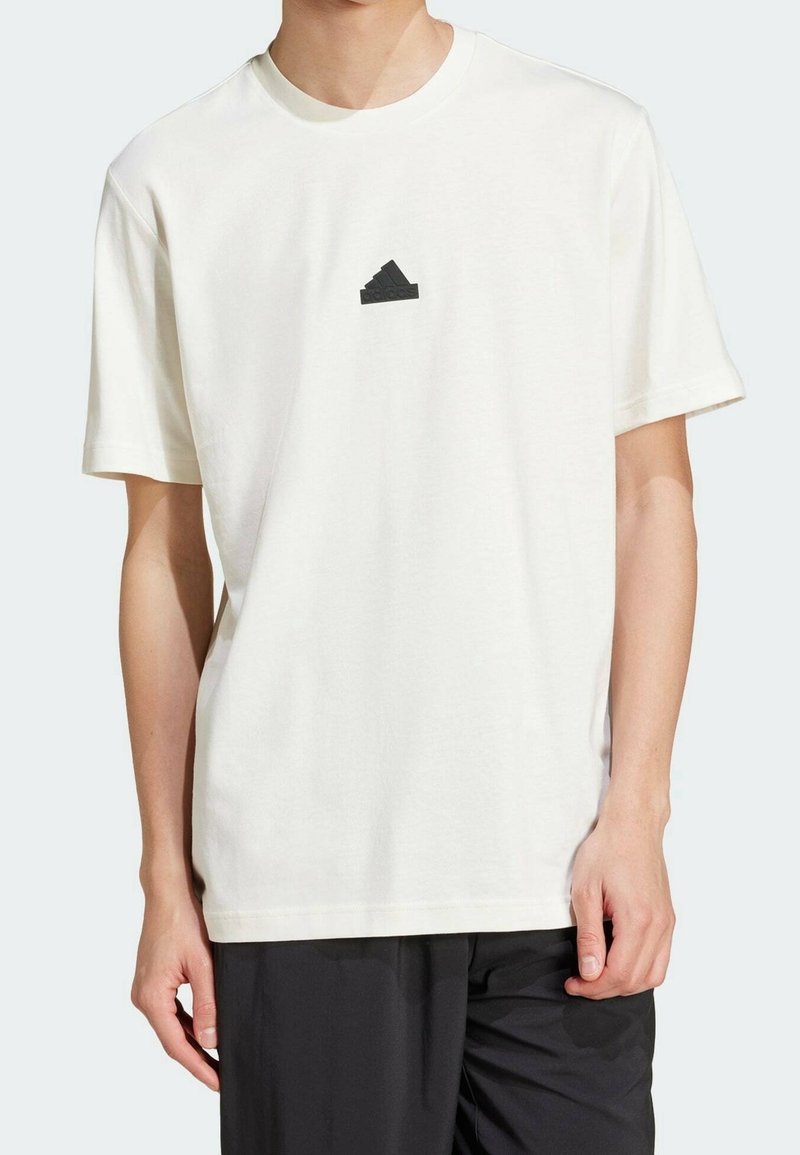 Camiseta de algodón blanca con mangas cortas y escote redondo. Presenta un logo de pirámide negra en el pecho. Textura suave y lisa.