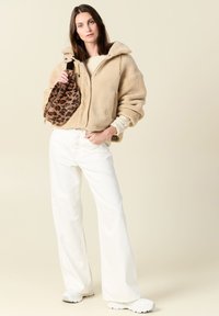 Giacca in felpa beige con zip, pantaloni bianchi larghi e sneakers bianche. La borsa ha una stampa leopardata, aggiungendo un accento texturizzato.