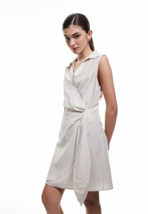 Helles beiges Wickelkleid mit einem kragenlosen Ausschnitt, kurzen Ärmeln und einem gebundenen Detail an der Taille. Hergestellt aus einem weichen, strukturierten Stoff.