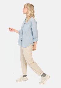 Hellblauses Hemd mit weißen Streifen, aus leichtem Material und mit langen Ärmeln. Kombiniert mit beigen Hosen und sichtbaren grauen Socken.