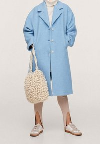 Abrigo de mezcla de lana azul claro con cuello de pico y tres botones. Bolso de mano de punto beige con un acabado texturizado. Leggings beige con canalé y zapatillas.