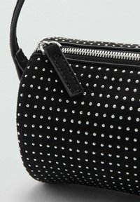 Bolso de ante negro con forma cilíndrica, detallado con tachuelas plateadas distribuidas uniformemente por toda la superficie y cierre de cremallera plateada.