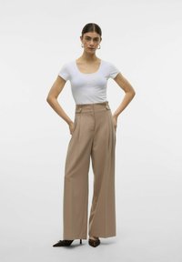Beige brede bukser med sidelommer, høj talje og knapdetaljer, parret med en tætsiddende hvid T-shirt med korte ærmer. Glat tekstur.