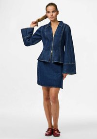 Temno modra denimska jakna z oprijetim krojem, zadrgo in zvonastimi rokavi, v kombinaciji z usklajenim denimsko krilom. Gladka tekstura, kontrastni šivi.