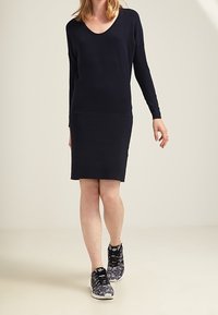 Robe en tricot bleu marine avec un col rond et des manches longues, associée à des baskets noires et blanches à motifs. Texture lisse, coupe à mi-genoux.