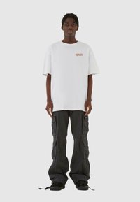Hvid oversized t-shirt med orange logo, parret med løse sorte cargo-bukser der har flere lommer og snore i bunden. Sorte sko.