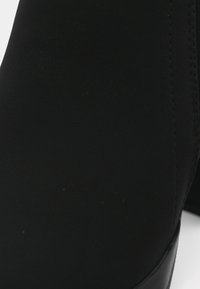 Gros plan sur le talon d'une chaussure en cuir noir avec des coutures visibles sur le côté et une surface texturée lisse.