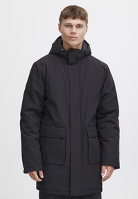Abrigo acolchado negro con capucha, dos bolsillos frontales, corte recto y textura suave, diseñado para proporcionar calidez en clima frío.