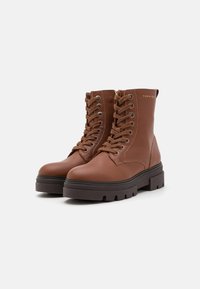 Brune lær ankle boots med en teksturert overflate, snøring, rund tå og en kraftig gummisåle. Har gulllogo på siden.