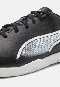 Černá sportovní obuv s texturovaným koženým svrškem, s bílými akcenty a tečkovaným vzorem po straně, a bílou gumovou podešví.