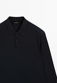 Schwarzes Langarm-Polohemd mit zwei Knöpfen und Kragen, Etikett mit "Massimo Dutti, Made in China", vor einem schlichten weißen Hintergrund.